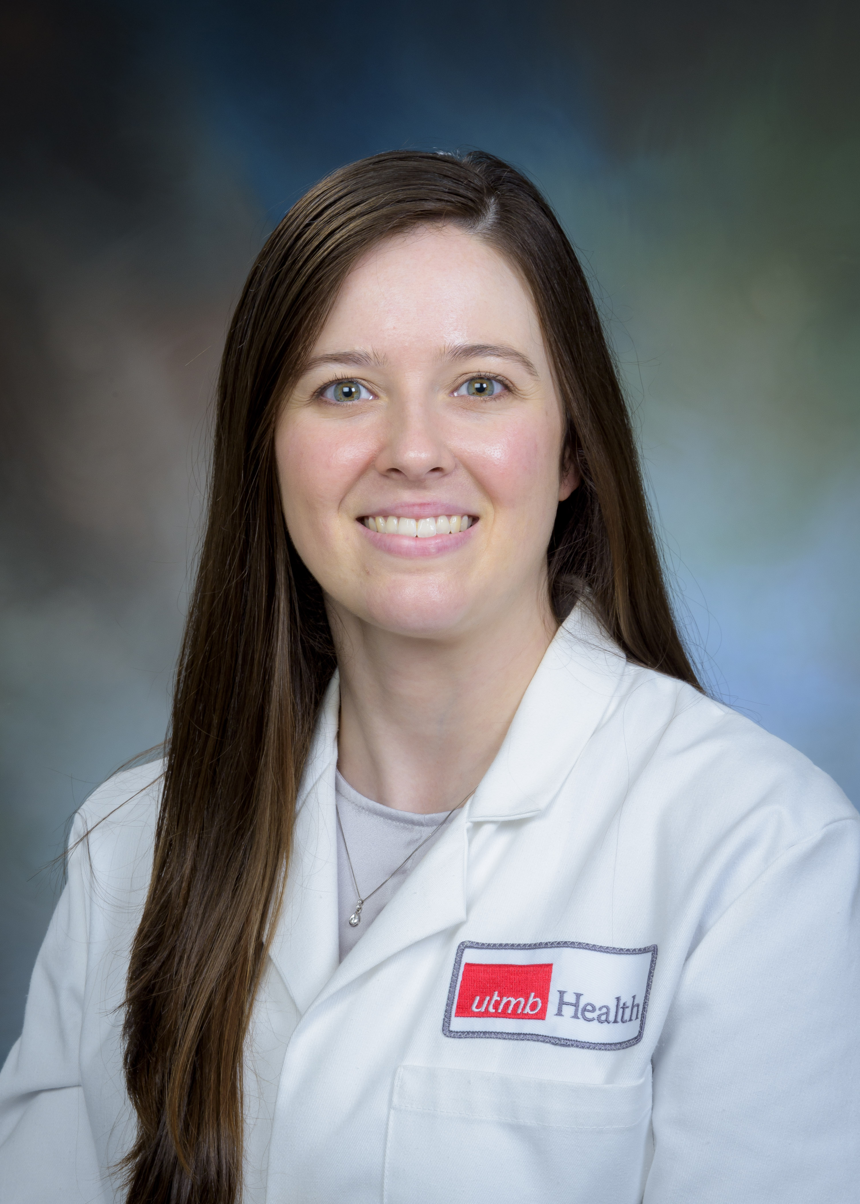 Studio portrait of a pharmacy preceptor wearing a white UTMB Health coat over a light top, photographed against a softly blended neutral background.