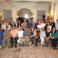 Large group of UTMB Alpha Omega Alpha members posing for a formal photo in an ornate room with chandeliers, decorative molding, and a patterned carpet, arranged in seated and standing rows.