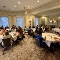 UTMB Alpha Omega attendees seated at multiple round tables engaged in group discussions in an ornate room with columns, chandeliers, decorative molding, and carpeted flooring.