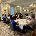 UTMB Alpha Omega participants seated at round tables engaged in group discussions in an ornate room with columns, chandeliers, fireplace, and patterned carpet.