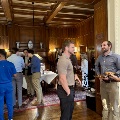 UTMB Alpha Omega Alpha group gathered indoors at a social event in a wood-paneled room, with attendees standing, conversing, and holding refreshments near tables with food and drinks.