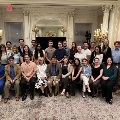 Large group of UTMB Alpha Omega Alpha members posing for a formal photo in an ornate room with chandeliers, decorative molding, and a patterned carpet, arranged in seated and standing rows.