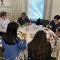Attendees seated around a round table eating and conversing at the Alpha Omega Alpha Texas Chapter UTMB 2022 Fall Mixer, with plates of food, drinks, and table signs labeled “Team #2” and “Team #7” in an ornate room.