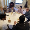 Attendees seated around a round dining table eating and conversing at the Alpha Omega Alpha Texas Chapter UTMB 2022 Fall Mixer, with a table sign reading “Team #4,” drinks, plates of food, and a presentation screen visible in the background.