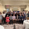 Large group of attendees posed together in an ornate indoor venue with decorative walls and chandeliers, seated and standing in rows during the Alpha Omega Alpha Texas Chapter UTMB 2022 Fall Mixer event; tables with drinks visible in foreground.