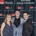 Three individuals stand together in front of a UTMB Health and John Sealy School of Medicine backdrop at the Alpha Omega Alpha 2023 Induction Ceremony, posing for a portrait.