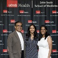 Three individuals stand together at the Alpha Omega Alpha 2023 Induction Ceremony at UTMB, posing in front of a UTMB Health and John Sealy School of Medicine backdrop with red and white balloon decorations at the side.