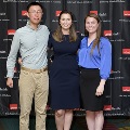 Three individuals pose together in front of a UTMB Health and John Sealy School of Medicine branded backdrop at the Alpha Omega Alpha 2023 Induction Ceremony, standing on a patterned carpeted floor.
