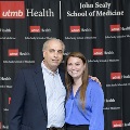 Two individuals stand together in front of a UTMB Health and John Sealy School of Medicine branded backdrop at the Alpha Omega Alpha 2023 Induction Ceremony, posing for a portrait.