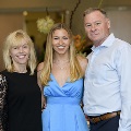 Three individuals pose together at the Alpha Omega Alpha 2023 Induction Ceremony at UTMB in a lobby setting, with decorative plants and glass doors visible in the background.