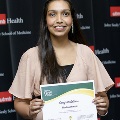 An individual holds a certificate reading “Congratulations Nadia Ahmed” at the Alpha Omega Alpha 2023 Induction Ceremony at UTMB, standing in front of a UTMB Health and John Sealy School of Medicine backdrop.