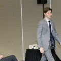 An individual in a gray suit walks across the front of a ballroom during the Alpha Omega Alpha 2023 Induction Ceremony at UTMB, while seated attendees nearby watch and applaud.