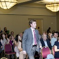 An individual walks down an aisle in a ballroom during the Alpha Omega Alpha 2023 Induction Ceremony at UTMB, with seated attendees watching on both sides under large overhead lights.