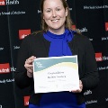 An individual holds a certificate reading “Congratulations Christine Crumbey” at the Alpha Omega Alpha 2023 Induction Ceremony at UTMB, standing in front of a UTMB Health and John Sealy School of Medicine backdrop.