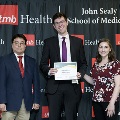Three individuals stand together at the Alpha Omega Alpha 2023 Induction Ceremony at UTMB, with one holding a certificate, posing in front of a UTMB Health and John Sealy School of Medicine backdrop.