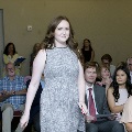 An individual walks down an aisle in a ballroom during the Alpha Omega Alpha 2023 Induction Ceremony at UTMB, with seated attendees on both sides watching and holding programs.