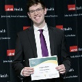 An individual holds a certificate reading “Congratulations Frederick Ditmars” at the Alpha Omega Alpha 2023 Induction Ceremony at UTMB, in front of a UTMB Health and John Sealy School of Medicine backdrop.