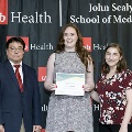 Three individuals stand together at the Alpha Omega Alpha 2023 Induction Ceremony at UTMB, with one holding a certificate in front of a UTMB Health and John Sealy School of Medicine backdrop.