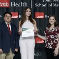 Three individuals pose together at the Alpha Omega Alpha 2023 Induction Ceremony at UTMB, with one holding a certificate in front of a UTMB Health and John Sealy School of Medicine branded backdrop.