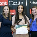 Three individuals pose together at the Alpha Omega Alpha 2023 Induction Ceremony at UTMB, with one holding a certificate in front of a UTMB Health and John Sealy School of Medicine logo backdrop.
