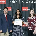 Three individuals stand together at the Alpha Omega Alpha 2023 Induction Ceremony at UTMB, with one holding a certificate in front of a UTMB Health and John Sealy School of Medicine branded backdrop.
