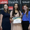 Three individuals pose together at the Alpha Omega Alpha 2023 Induction Ceremony at UTMB, with one holding a certificate in front of a UTMB Health and John Sealy School of Medicine backdrop.