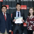 Three individuals stand together at the Alpha Omega Alpha 2023 Induction Ceremony at UTMB, with one holding a certificate in front of a UTMB Health and John Sealy School of Medicine logo backdrop.