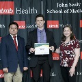 An individual holds a certificate reading “Congratulations Frederick Ditmars” at the Alpha Omega Alpha 2023 Induction Ceremony at UTMB, in front of a UTMB Health and John Sealy School of Medicine backdrop.
