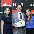 Three individuals pose together at the Alpha Omega Alpha 2023 Induction Ceremony at UTMB, with one holding a certificate in front of a UTMB Health and John Sealy School of Medicine branded backdrop.