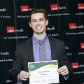 An individual holds a certificate and smiles for a portrait at the Alpha Omega Alpha 2023 Induction Ceremony at UTMB, in front of a UTMB Health and John Sealy School of Medicine backdrop.