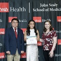 Three individuals stand together at the Alpha Omega Alpha 2023 Induction Ceremony at UTMB, posing in front of a UTMB Health and John Sealy School of Medicine logo backdrop.