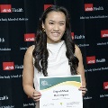 An individual holds a certificate reading “Congratulations Chelsea Nguyen” at the Alpha Omega Alpha 2023 Induction Ceremony at UTMB, standing in front of a UTMB Health and John Sealy School of Medicine backdrop.