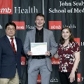 Three individuals pose together at the Alpha Omega Alpha 2023 Induction Ceremony at UTMB, with one holding a certificate in front of a UTMB Health and John Sealy School of Medicine branded backdrop.