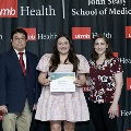 Three individuals pose together at the Alpha Omega Alpha 2023 Induction Ceremony at UTMB, with one holding a certificate in front of a UTMB Health and John Sealy School of Medicine backdrop.