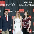 Three individuals pose together at the Alpha Omega Alpha 2023 Induction Ceremony at UTMB, standing in front of a UTMB Health and John Sealy School of Medicine logo backdrop, with one individual wearing green honor cords.