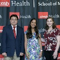 Three individuals pose together at the Alpha Omega Alpha 2023 Induction Ceremony at UTMB, standing in front of a UTMB Health and John Sealy School of Medicine branded backdrop.
