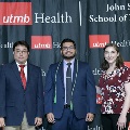 Three individuals stand together at the Alpha Omega Alpha 2023 Induction Ceremony at UTMB, posing in front of a UTMB Health and John Sealy School of Medicine logo backdrop, with one individual wearing green honor cords.