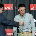 An individual places green honor cords around another individual’s neck during the Alpha Omega Alpha 2023 Induction Ceremony at UTMB, with a UTMB Health and John Sealy School of Medicine backdrop behind them.
