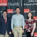 Three individuals pose together at the Alpha Omega Alpha 2023 Induction Ceremony at UTMB, standing in front of a UTMB Health and John Sealy School of Medicine backdrop with repeating logos.