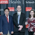 Three individuals stand together at the Alpha Omega Alpha 2023 Induction Ceremony at UTMB, posing in front of a UTMB Health and John Sealy School of Medicine logo backdrop, with one individual wearing honor cords.