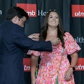 An individual places green honor cords around another individual’s neck during the Alpha Omega Alpha 2023 Induction Ceremony at UTMB, with a UTMB Health and John Sealy School of Medicine branded backdrop behind them.