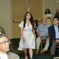 An individual walks forward holding a program during the Alpha Omega Alpha 2023 Induction Ceremony at UTMB, with seated attendees and a banquet hall setting visible in the background.