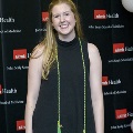 An individual stands for a portrait at the Alpha Omega Alpha 2023 Induction Ceremony at UTMB, wearing green honor cords in front of a UTMB Health and John Sealy School of Medicine backdrop with balloon decorations.