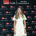 An individual stands for a portrait at the Alpha Omega Alpha 2023 Induction Ceremony at UTMB, wearing a light-colored dress in front of a UTMB Health and John Sealy School of Medicine branded backdrop.