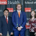 Three individuals stand together at the Alpha Omega Alpha 2023 Induction Ceremony at UTMB, posing in front of a UTMB Health and John Sealy School of Medicine logo backdrop.