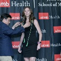 An individual places honor cords around another individual’s neck during the Alpha Omega Alpha 2023 Induction Ceremony at UTMB, with a UTMB Health and John Sealy School of Medicine backdrop behind them.