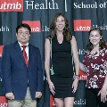 Three individuals pose together at the Alpha Omega Alpha 2023 Induction Ceremony at UTMB, standing in front of a UTMB Health and John Sealy School of Medicine logo backdrop.