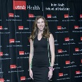 An individual stands for a portrait at the Alpha Omega Alpha 2023 Induction Ceremony at UTMB, wearing honor cords in front of a UTMB Health and John Sealy School of Medicine branded backdrop.