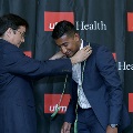 An individual places green honor cords around another individual’s neck during the Alpha Omega Alpha 2023 Induction Ceremony at UTMB, in front of a UTMB Health and John Sealy School of Medicine backdrop.