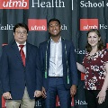 Three individuals stand together at the Alpha Omega Alpha 2023 Induction Ceremony at UTMB, posing in front of a UTMB Health and John Sealy School of Medicine branded backdrop.